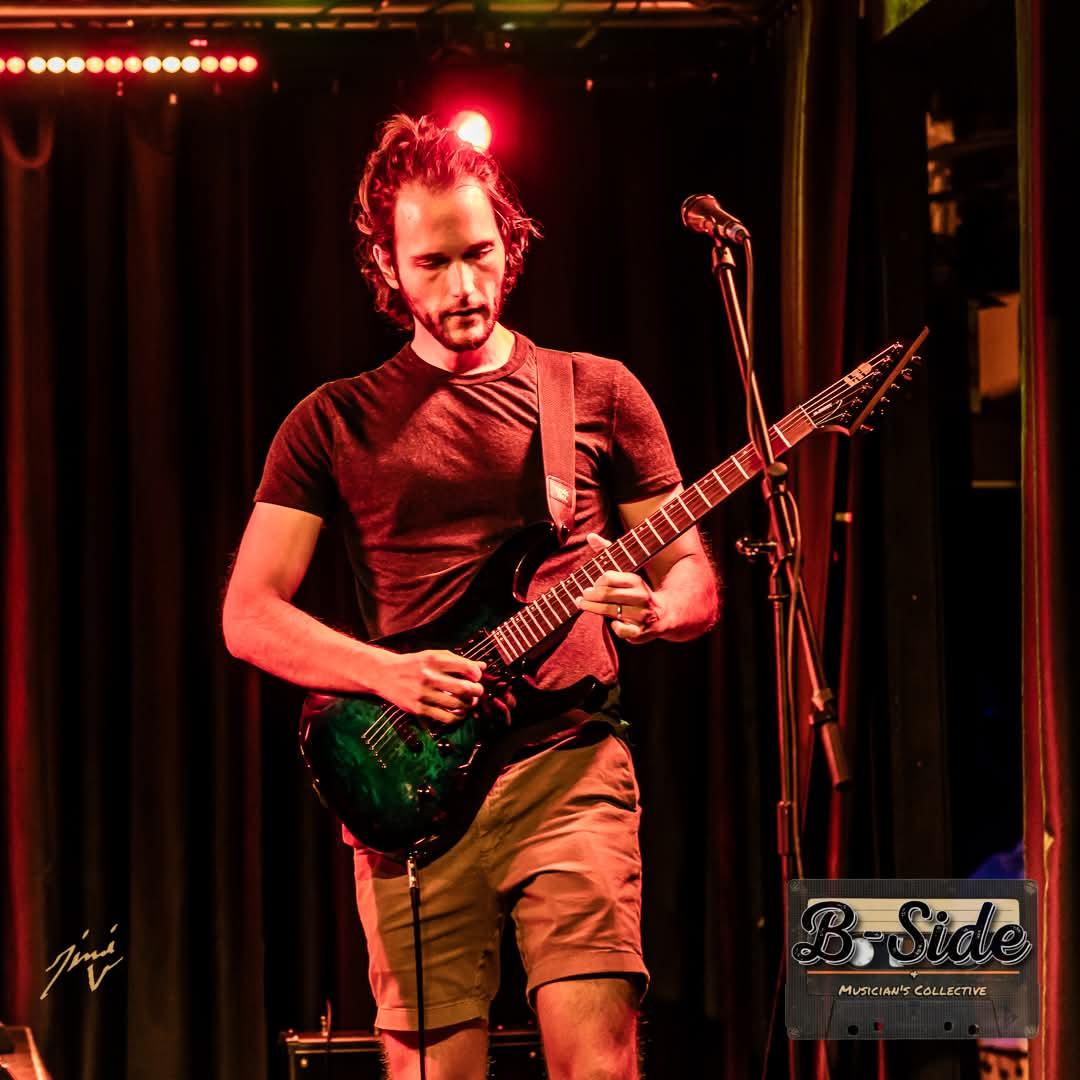 Tony playing a green electric guitar on stage under red lights